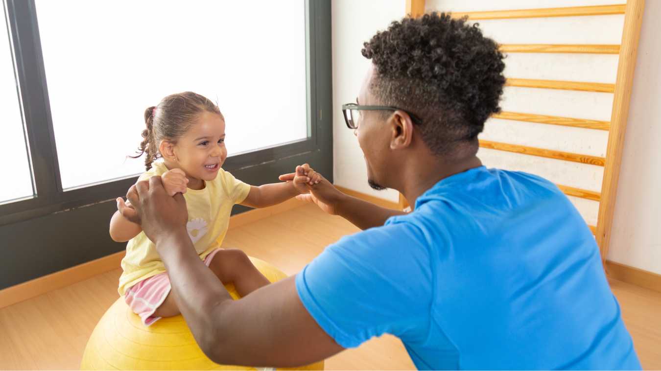 caregiver holding the hands of a young girl seated in front of him